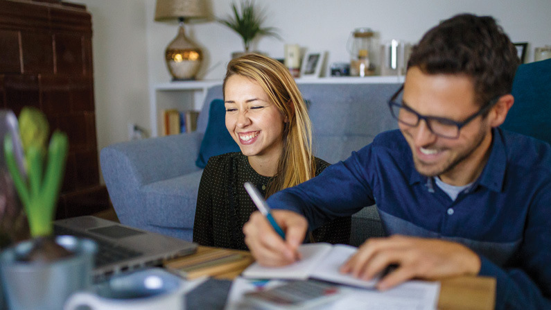 Young couple sitting together. Man writing in notebook.