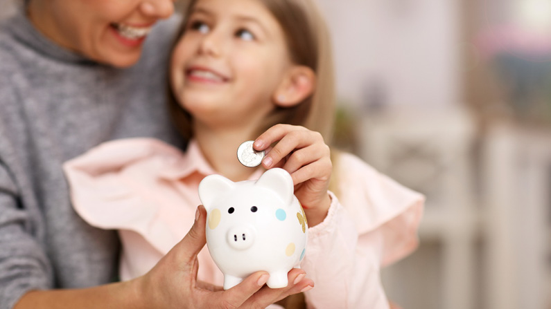 Mom and daughter putting coins in piggy bank