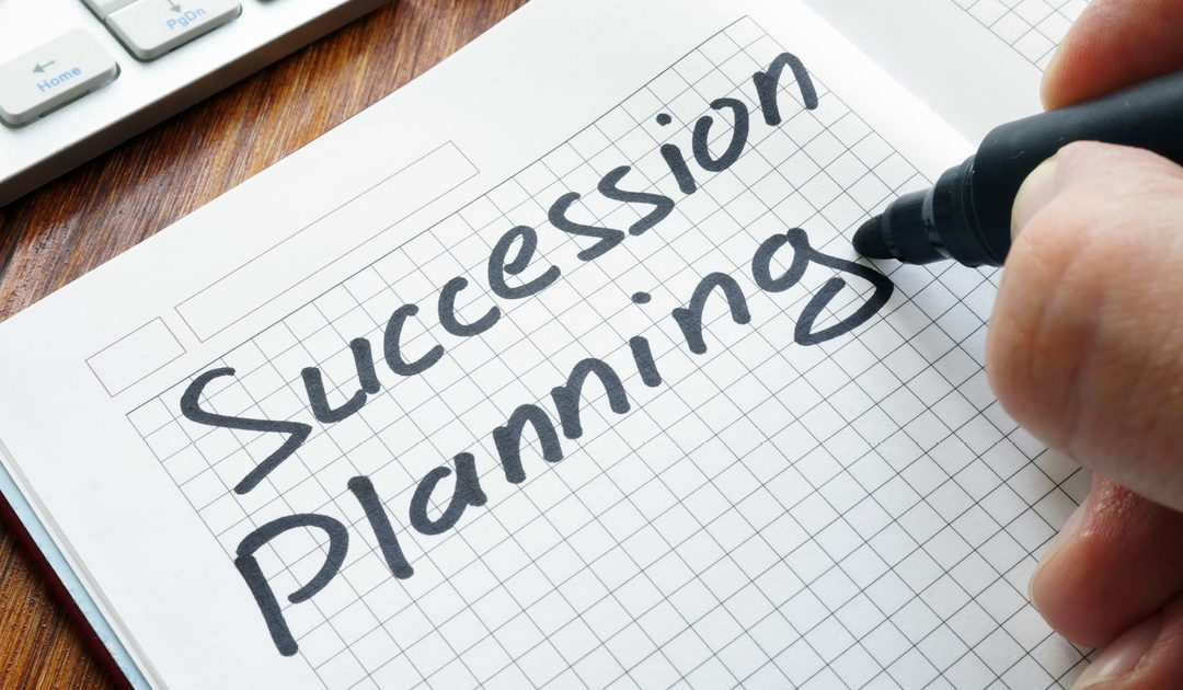Person writing 'succession planning' on piece of paper