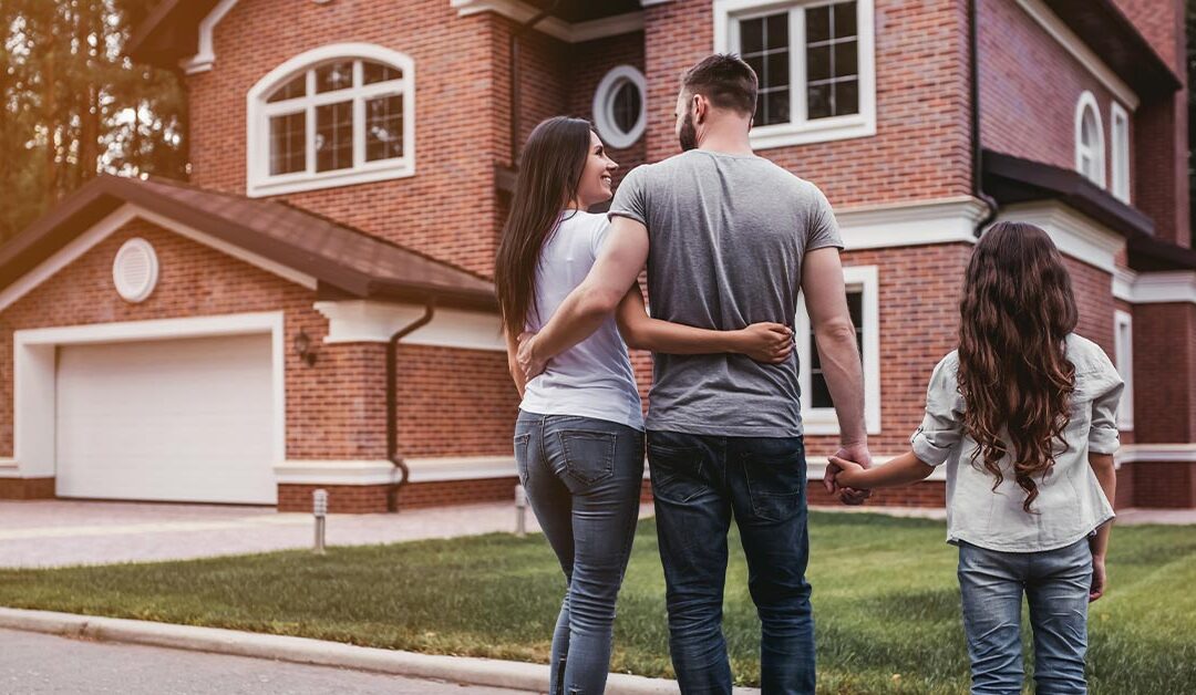 Husband, wife and child standing in front of their home